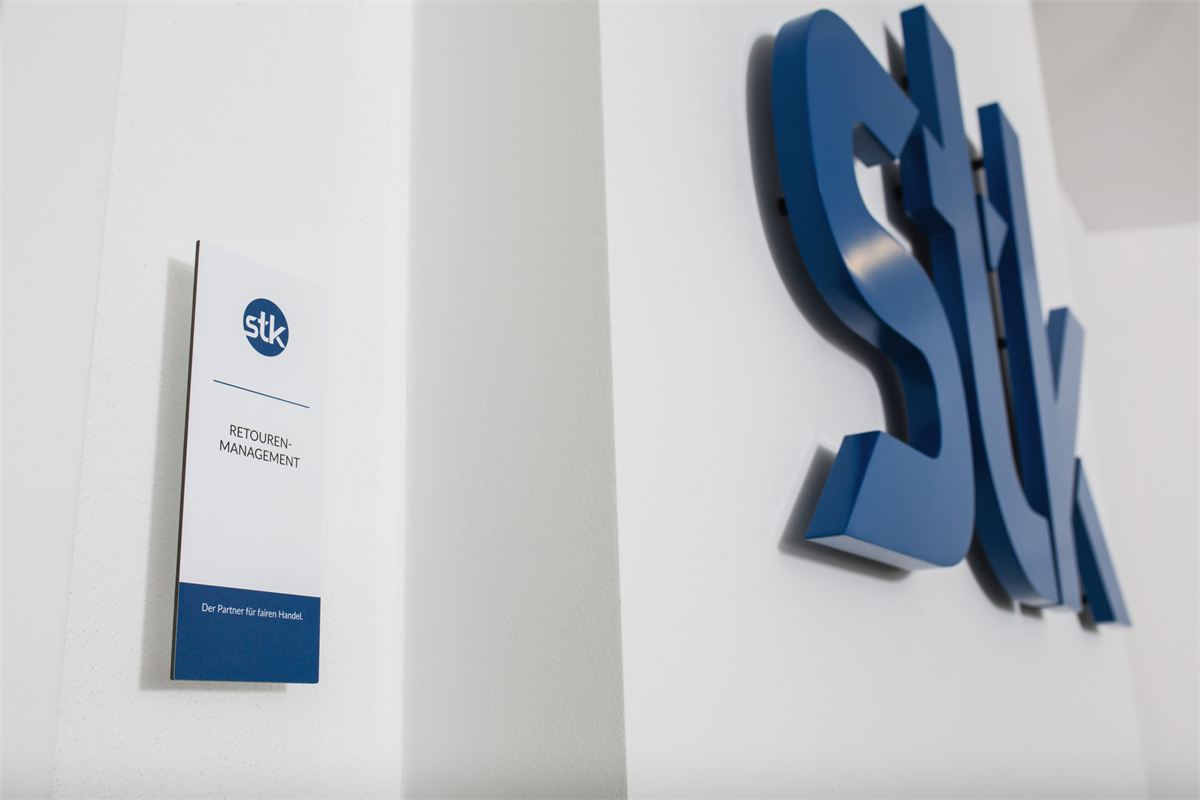 Türschild „Retourenmanagement“ neben dem STK-Logo am Firmensitz in Schönberg