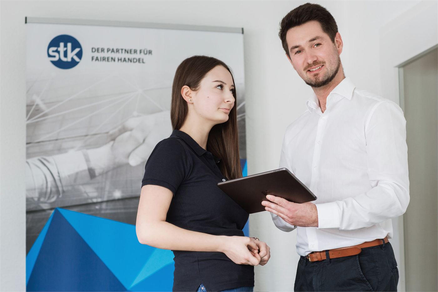 Zwei Mitarbeitende der STK AG im Gespräch vor einem Banner mit der Aufschrift „Der Partner für fairen Handel“